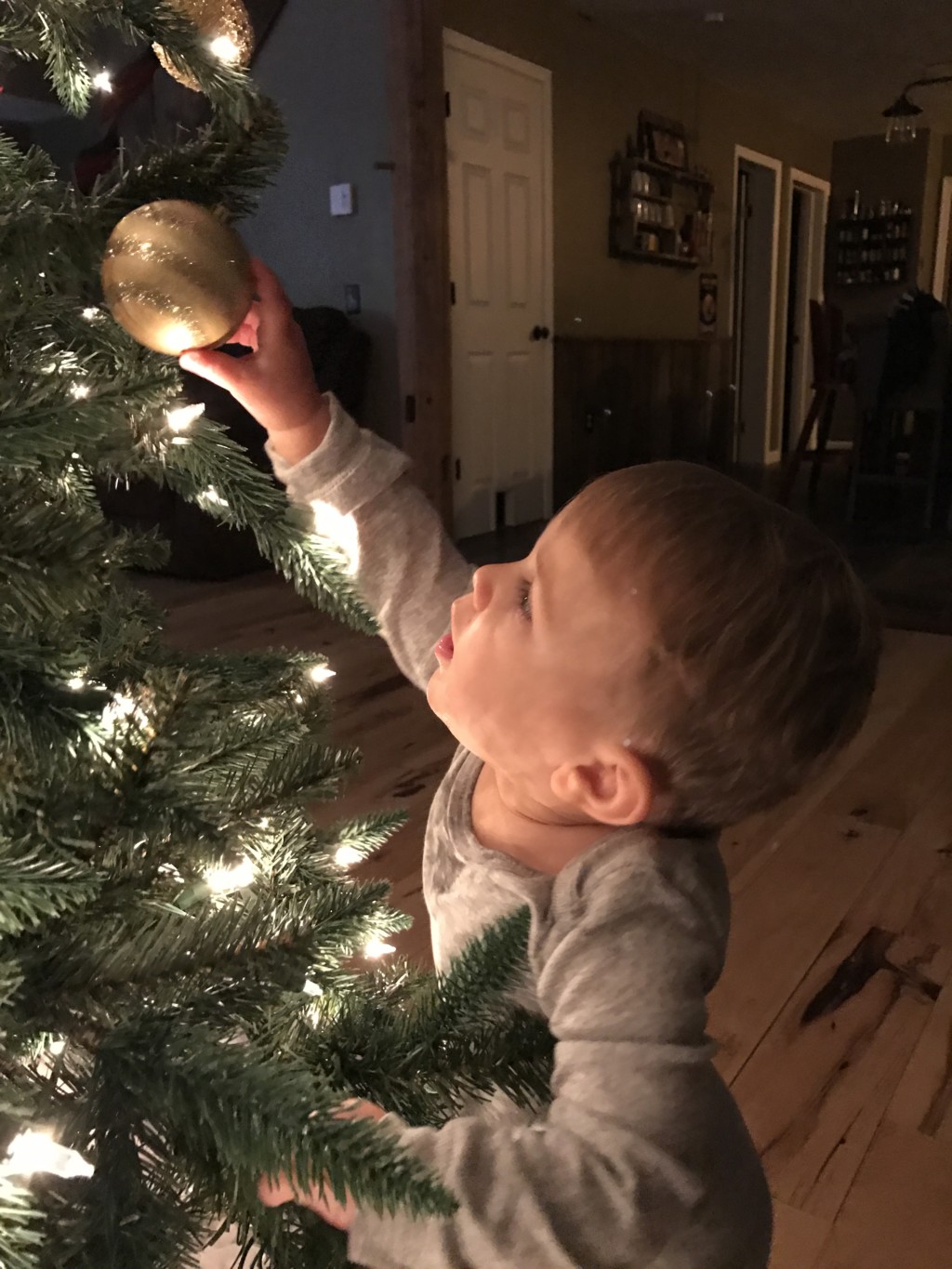 Child reaching for Christmas ornaments on Christmas tree
