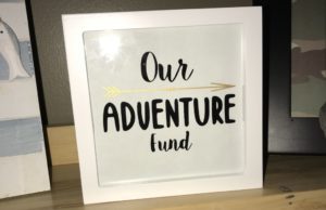 White shadow box used as a piggy bank with "Our Adventure Fund" written on the front