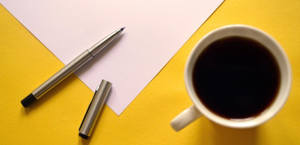 Paper and pen on yellow table with black coffee on the side