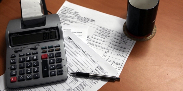 Tax documents, calculator, and coffee mug on a desk.