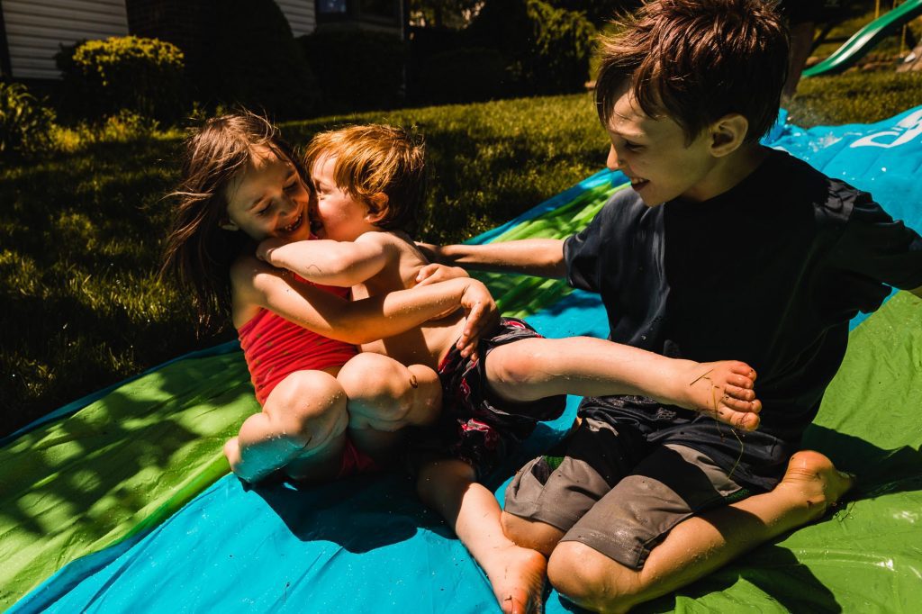 kids sliding on a summer waterslide in the backyard, hugging and laughing together