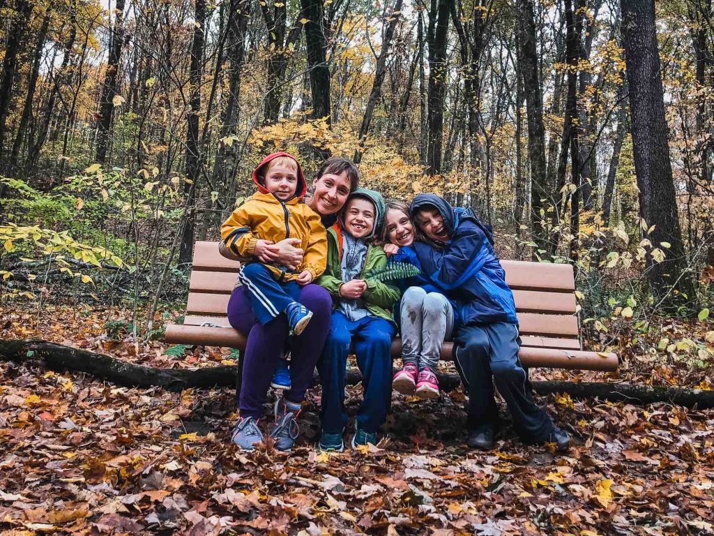 mom and four kids cuddled together outside on a bench smiling