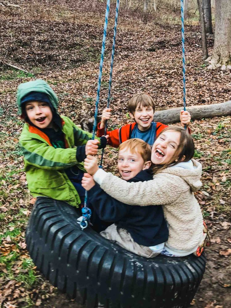 kids swinging on a tire swing outside in nature in the cold weather