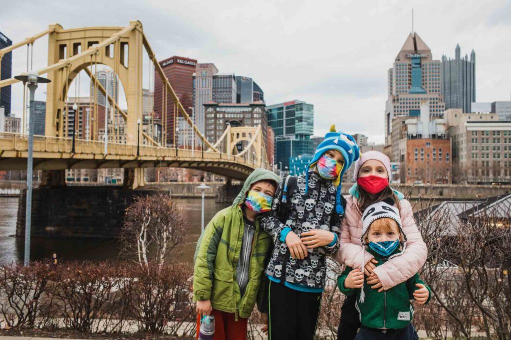 kids wearing masks standing in front of the city of pittsburgh and the roberto clemente bridge